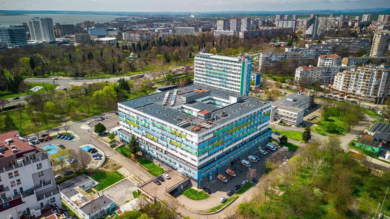 Spitalul municipal din orașul Burgas, Bulgaria, văzut de sus cu drona. În parcare se văd câteva mașini de ambulanță, copaci și alte clădiri în jur, iar în spate este marea.