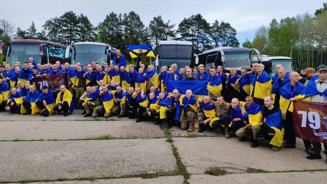 Poză cu soldații ucraineni eliberați marți, 6 mai, în cadrul schimbului de prizonieri dintre Rusia și Ucraina. Țin în mâini steaguri ale Ucrainei și sunt așezați în fața a cinci autocare