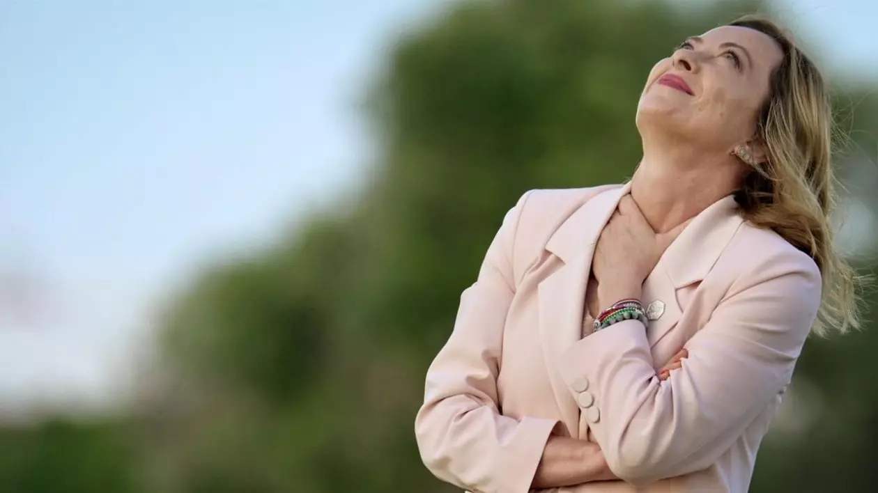 Premierul italian Georgia Meloni în mijlocul naturii, îmbrăcată într-un costum roz piersică, cu capul pe spate, părul fluturând si mâna stangă pusă la gat