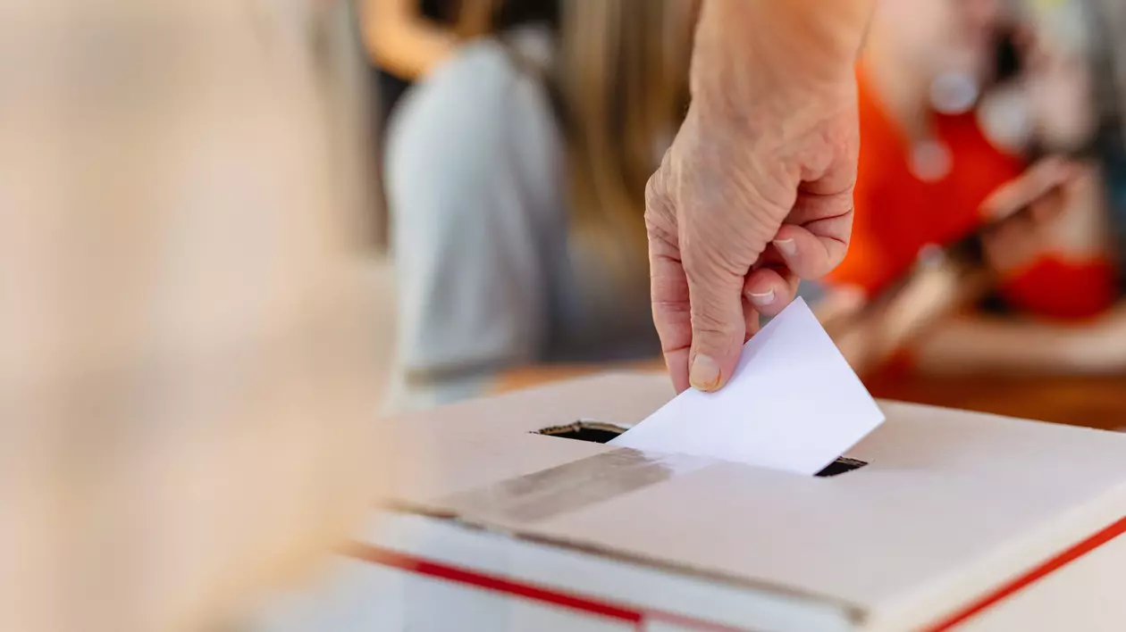 Poza din sala de votara cu mana unei persoane care baga fluturasul de votare in urna