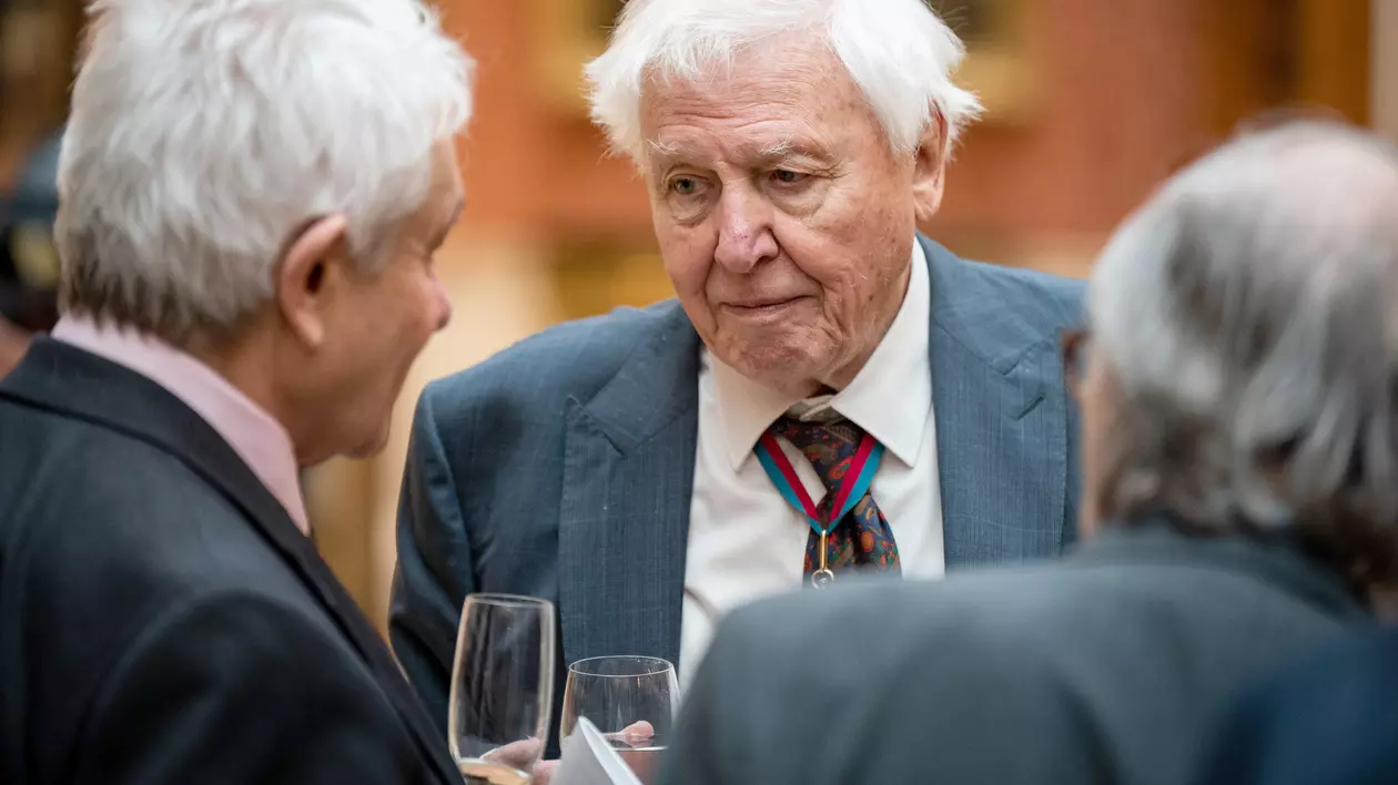 Naturalistul Sir David Attenborough, la un prânz, cu un pahar inn mână discutând cu două persoane