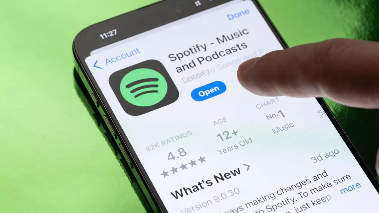 Pagina Spotify din AppStore, deschisă pe ecranul unui iPhone așezat deasupra unui fundal verde.