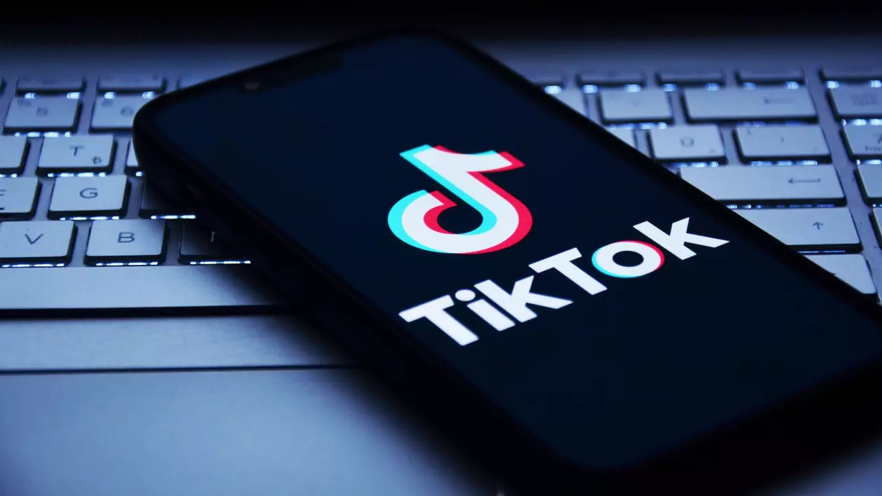 Telefon mobil pe care este deschisă aplicația TikTok. Este așezat pe tastatura unui laptop