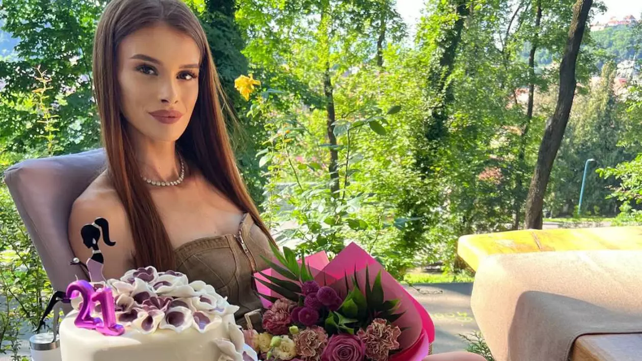Teodora Marcu de la Insula iubirii îmbrăcată într-o rochie maro, pe o terasa la un restaurant cu un tort în mână, în ziua în care a împlinit 21 de ani.
