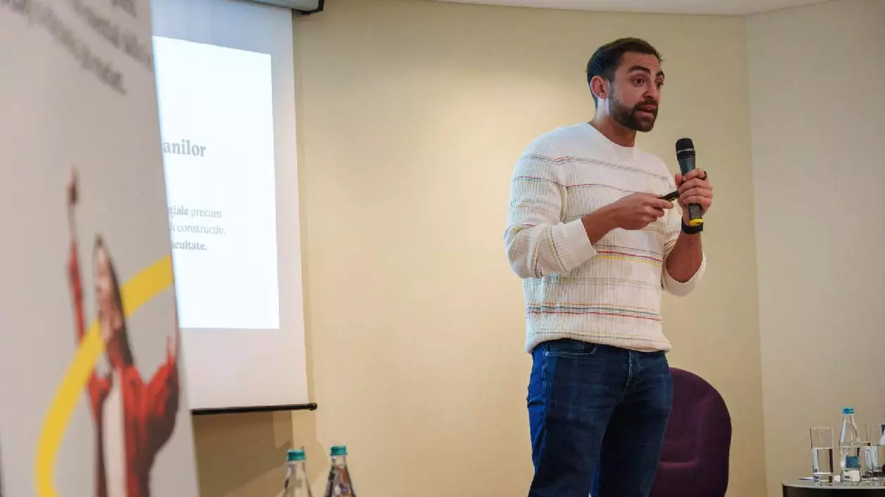 Tânăr care stă în picioare, are un microfon în mână și se adresează unei audiențe