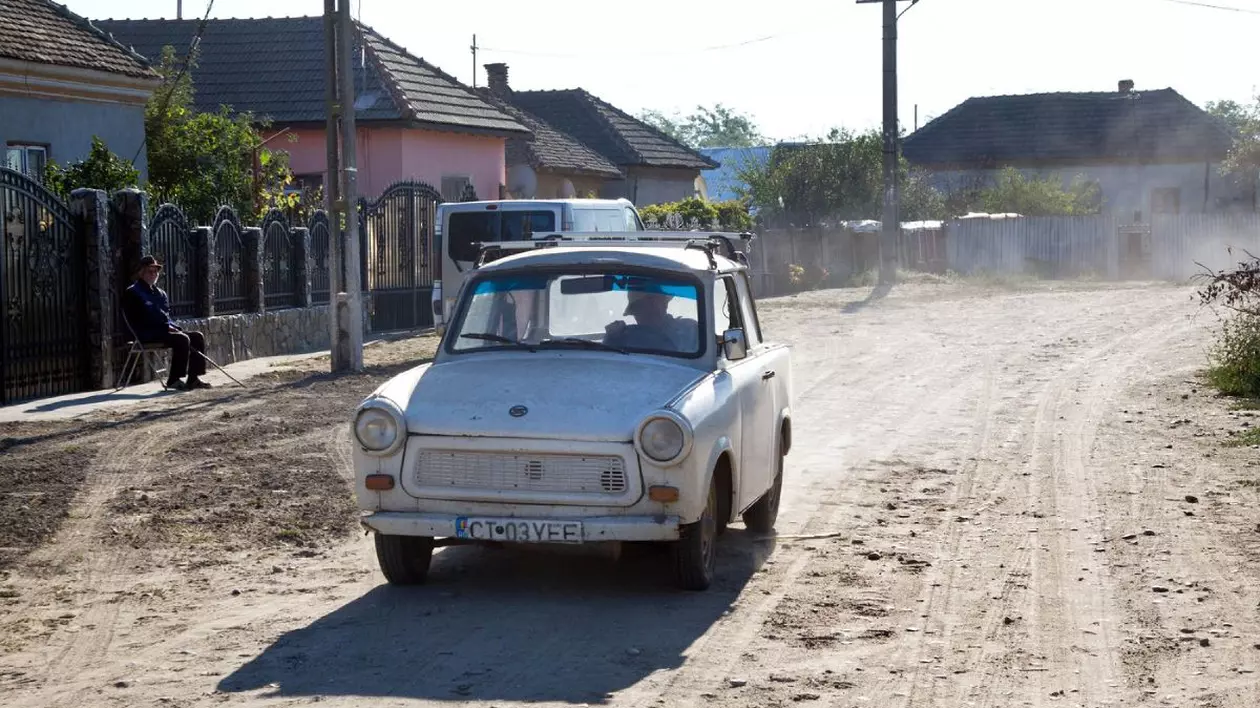 Trabant vechi, de culoare deschisă, pe o stradă neasfaltată, în timp ce scoate fum, în satul Piscu Vechi din județul Dolj