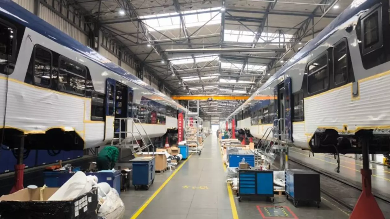 Interiorul unei fabrici feroviară, unde sunt asamblate vagoane de tren electrice. În imagine sunt două garnituri mari în faza de asamblare.