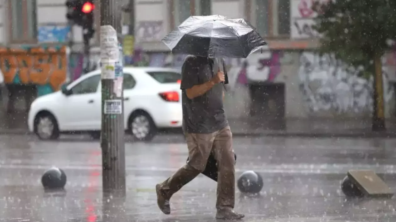 În imagine este ilustrat un bărbat care merge pe o stradă, în timp ce plouă. Acesta ține o umbrelă deasupra capului.