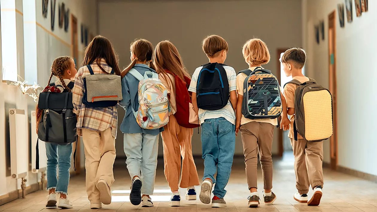 Un grup de școlari cu ghiozdane se plimbă pe coridorul școlii în timpul pauzei.