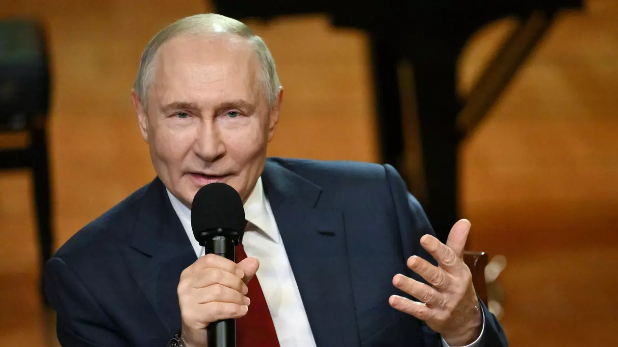 Vladimir Putin vorbește la microfon. Este îmbrăcat într-un sacou negru, cămașă albă și cravată vișinie.