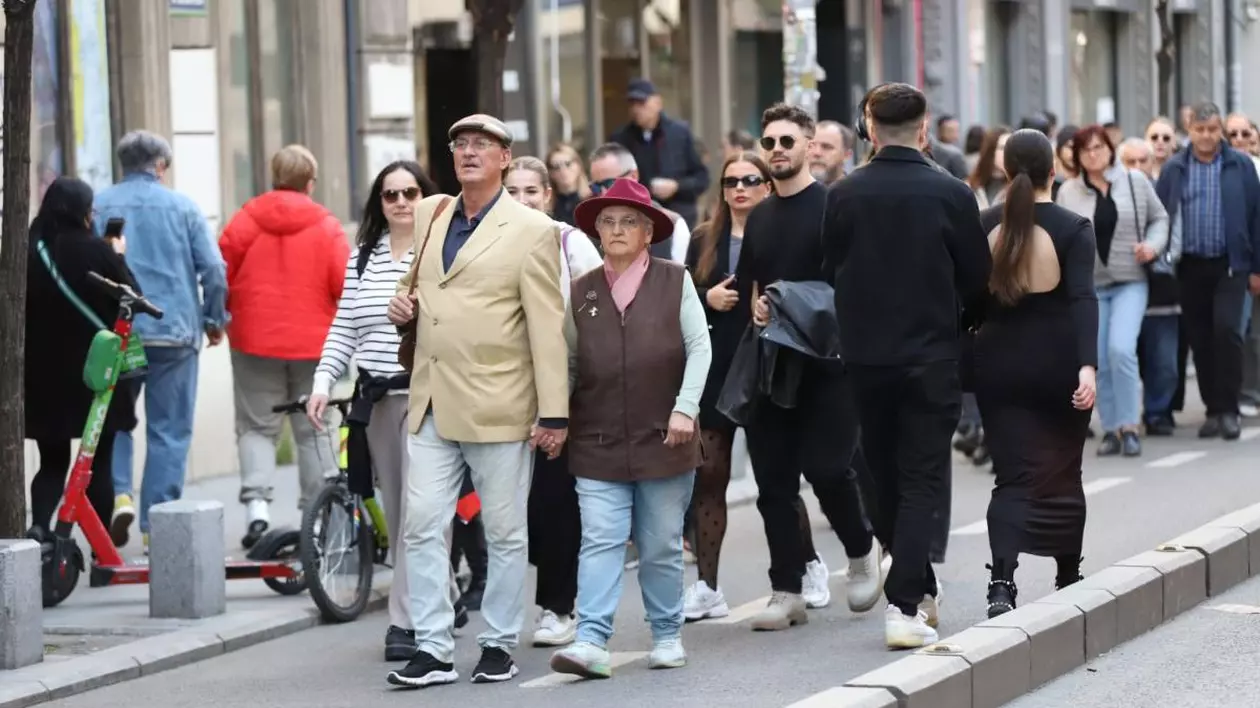 Mai mulți oameni se plimbă pe stradă, unii îmbrăcați cu geci, iar în prim-plan se vede un cuplu de pensionari și în spatele lor, mulți tineri, pe Calea Victoriei, București, 13 aprilie 2025.
