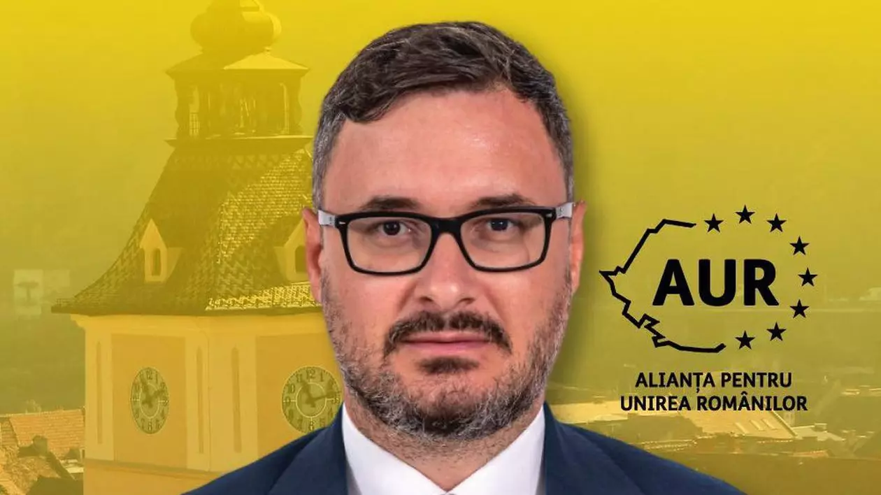 Dan Tanasă, purtător de cuvânt al AUR, îmbrăcat la costum, având în fundal o imagine din centrul orașului Brașov