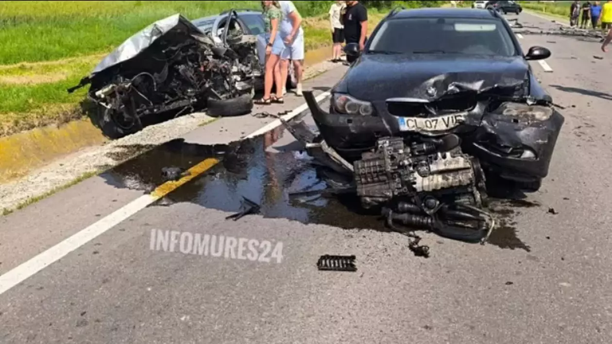 O mașină neagră, lovită în față, în prim-plan, în partea stângă sunt alte două autoturisme lovite pe margine și oameni lângă ele, iar în dreapta se văd alți martori, Brașov, Rupea, 7 iunie 2025