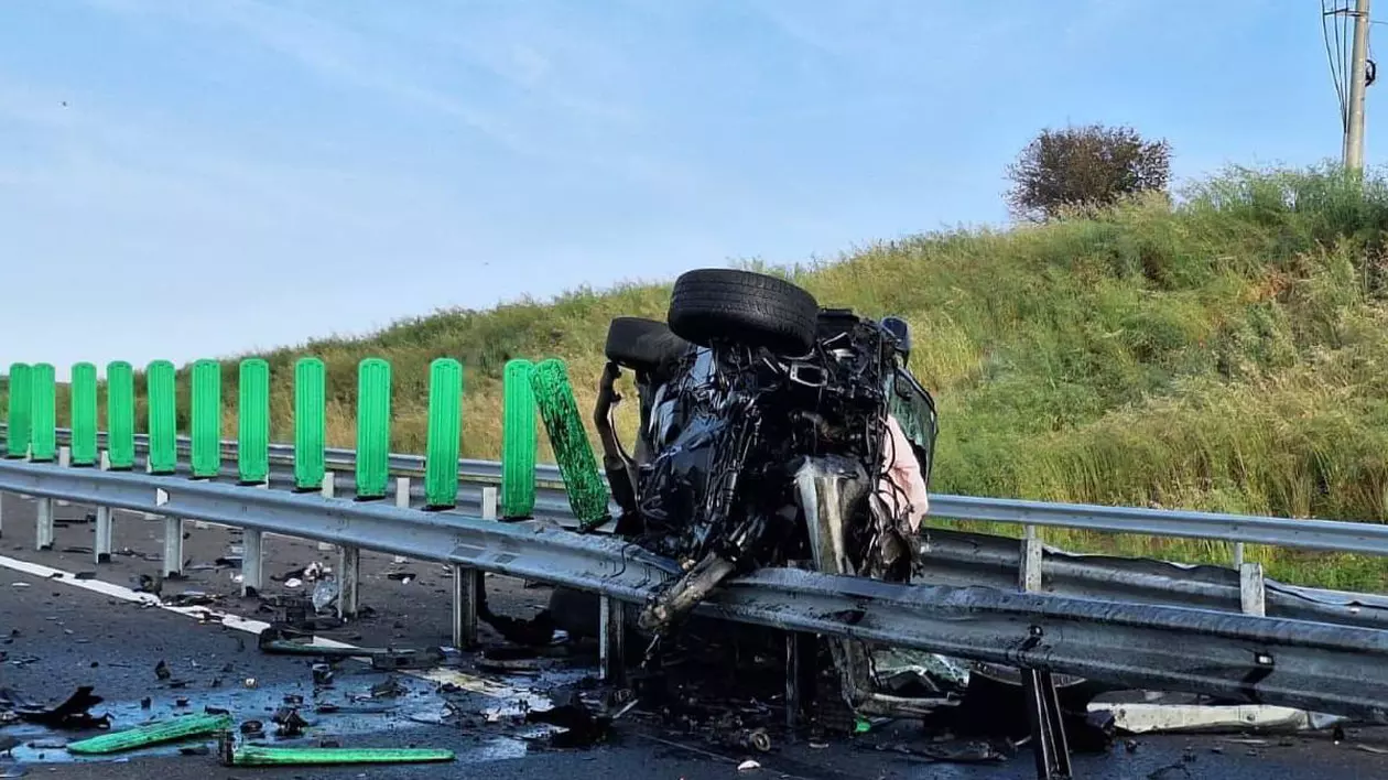 O mașină distrusă complet e lipită peste balustrada drumului expres ca o cutie de tinichea turtită