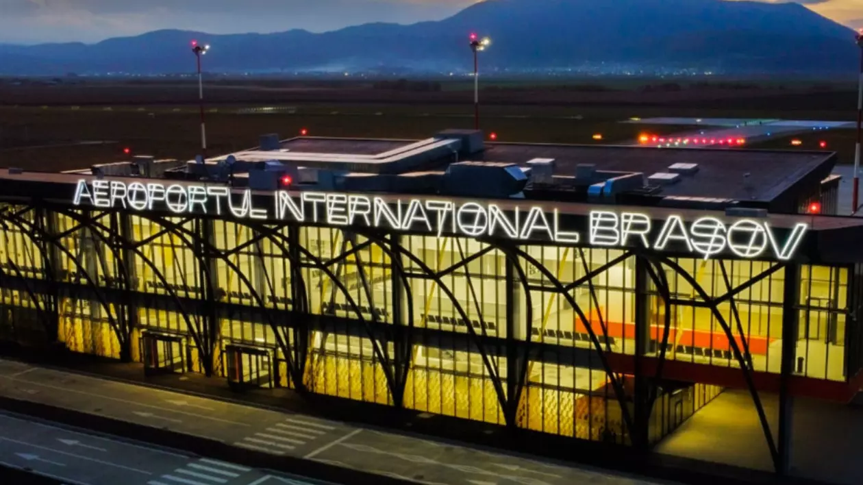 Imaginea prezintă clădirea principală a Aeroportului Internațional Brașov-Ghimbav. Numele aeroportului este afișat proeminent, cu litere mari luminate, vizibile de la distanță.