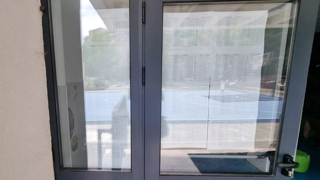 un panou de sticla de la o scoala cu foi lipite. este vorba de afisarea rezultatelor la bacalaureat 2025