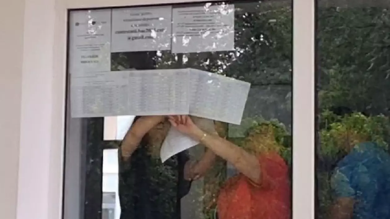 in imagine se vad trei persoane care lipesc pe frontul de sticla al unui liceu foi cu rezoltatele la bac 2025