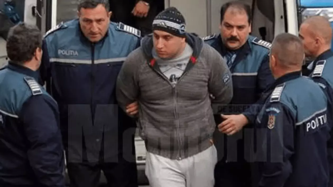 Alexandru Huțuleac este escortat de mai mulți polițiști. Acesta poartă un hanorac gri, pantaloni sport albi și o căciulă