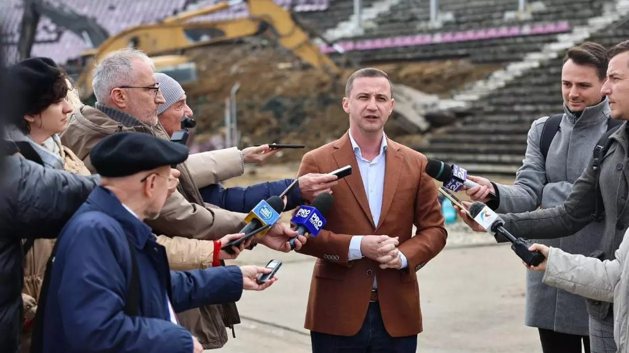 Alfred Simonis surprins în timp ce vorbește în fața jurnaliștilor, așezați și în stânga și în dreapta.