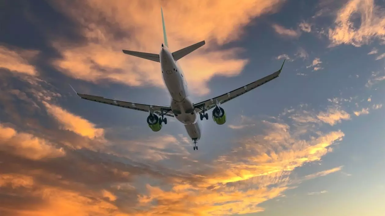 Un avion care zboară cu botul în sus, pe cer unde se văd câțiva nori la răsărit