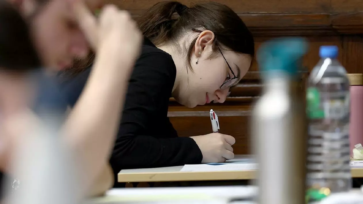 O elevă în prim plan, scrie pe o foiae, in imagine se vad sticle de apa. - Elevii susțin proba de filosofie în cadrul examenelor de bacalaureat, prima sesiune de testare a bacalaureatului 2024 (examen de absolvire a liceului) la liceul Fustel de Coulanges din Strasbourg, estul Franței, pe 18 iunie 2024.