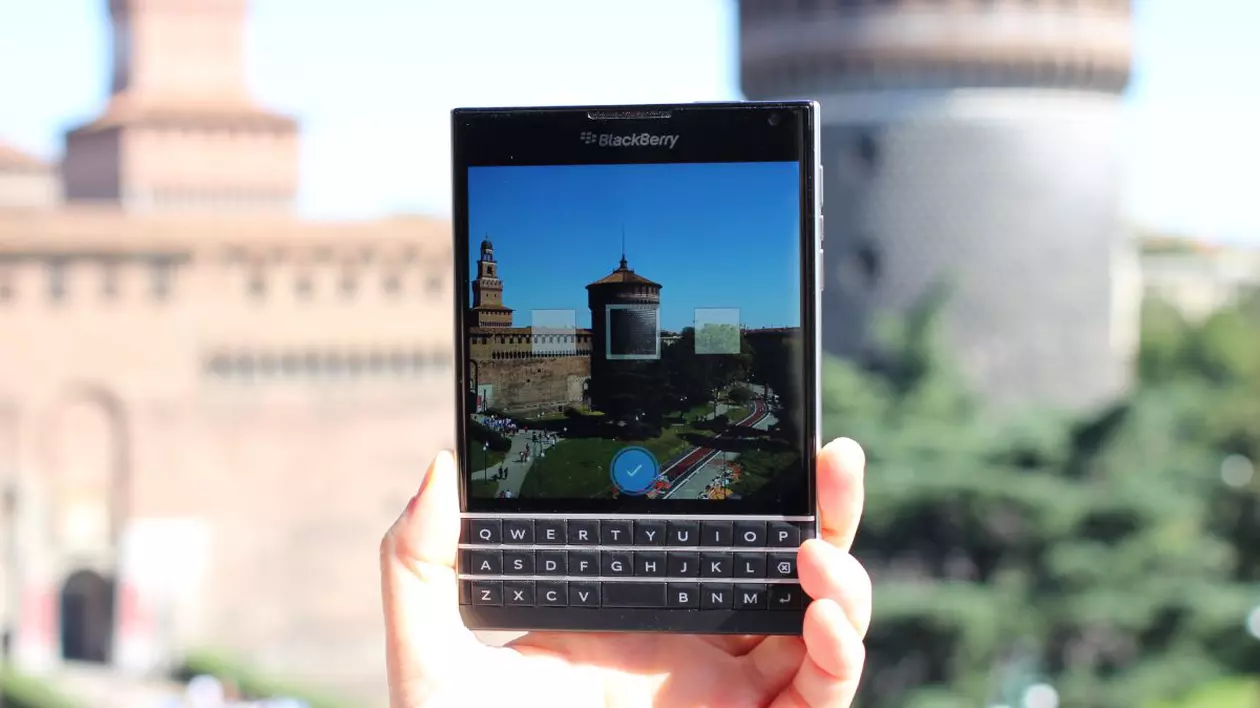 Un telefon BlackBerry Passport, ținut în mână de o persoană în fața unui castel din Italia.