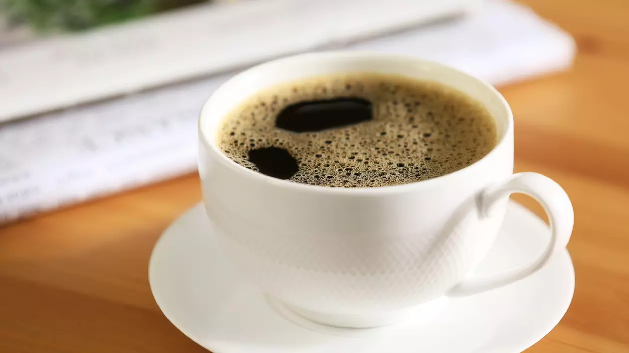 O ceașca albă cu cafea, pe o farfurie albă, așezate pe o masă din lemn.