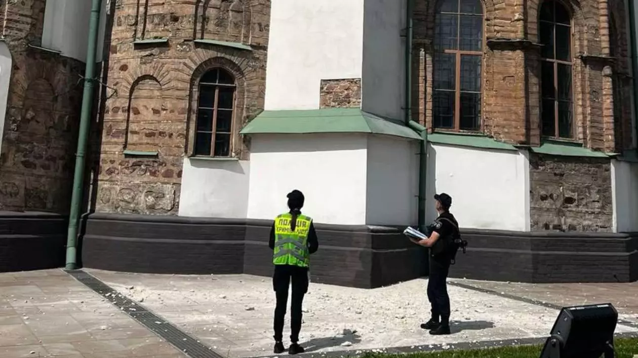 Doi angajați veniți în fața Catedralei Sfânta Sofia să analizeze pagubele după loviturile asupra Kievului, se vede pe asfalt cum bucăți din fațada clădirii au căzut.