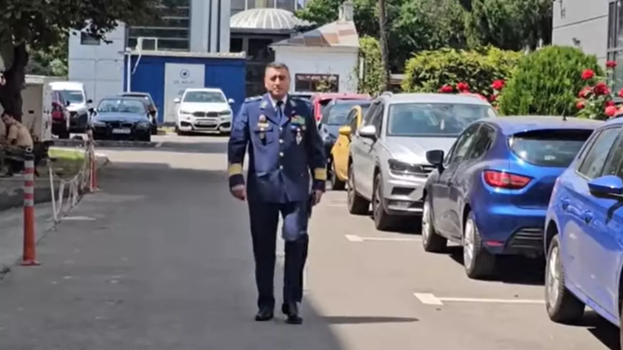 În imagine este un bărbat în uniformă militară, care merge pe o alee între mașini parcate.