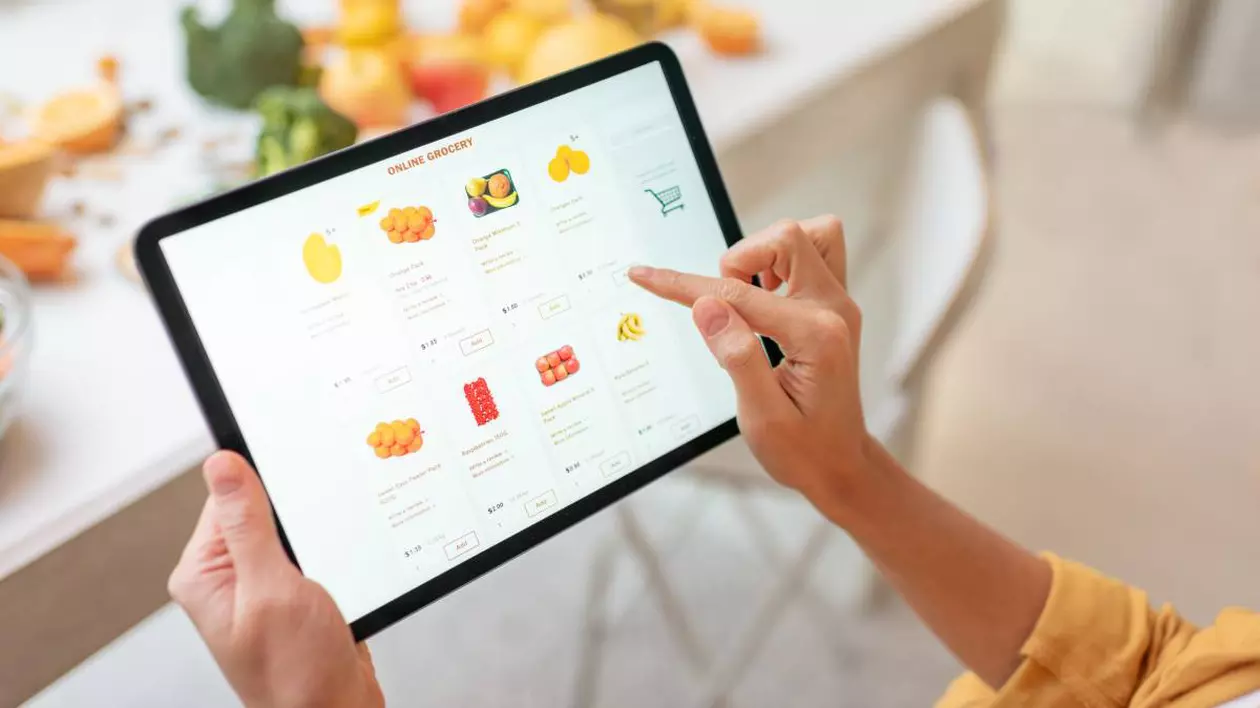 O femeie cu o tabletă în mână, în timp ce face cumpărături online și comandă fructe dintr-o aplicație.