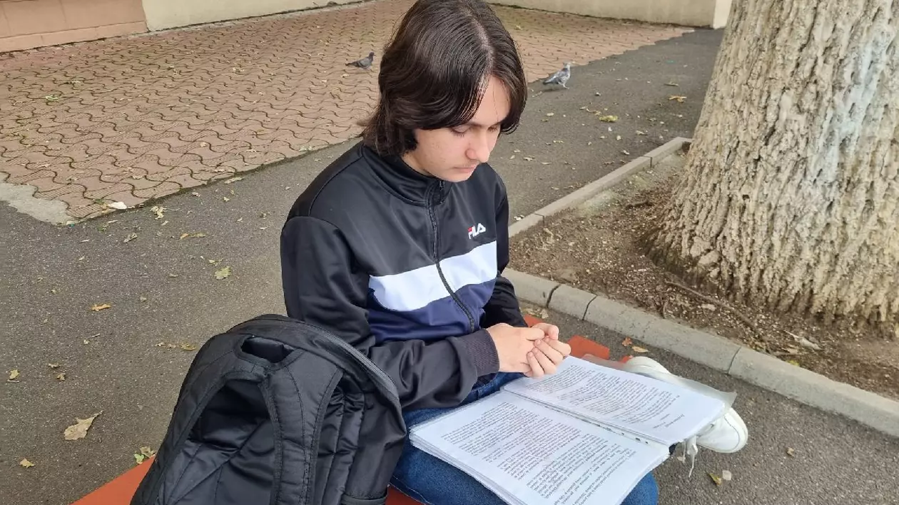 Un elev cu părul lung, sta pe o banca, cu un dosar deschis in fata, cu ghiozdanul negru, langa el, Isi frange mainile. Prima zi de BAC 2025
