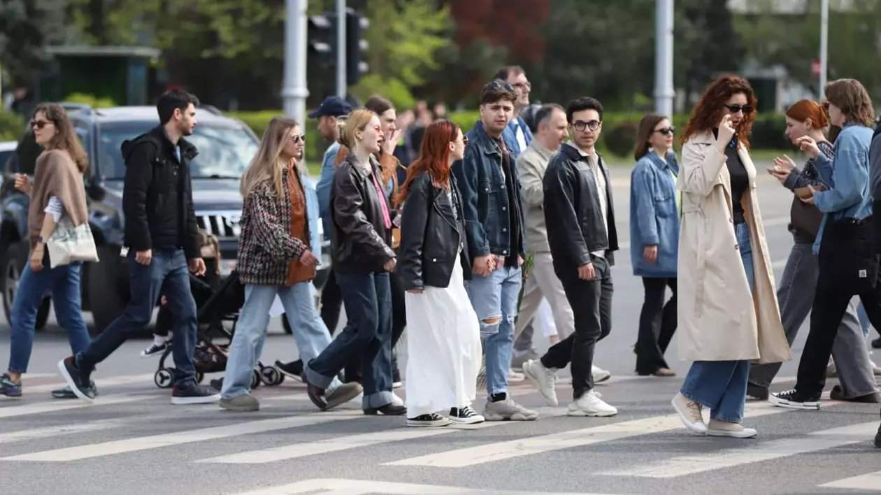 Mai mulți oameni îmbrăcați cu geci traversează strada pe trecerea de pietoni, iar în spate se vede o mașină de teren neagră, București, 13 aprilie 2025
