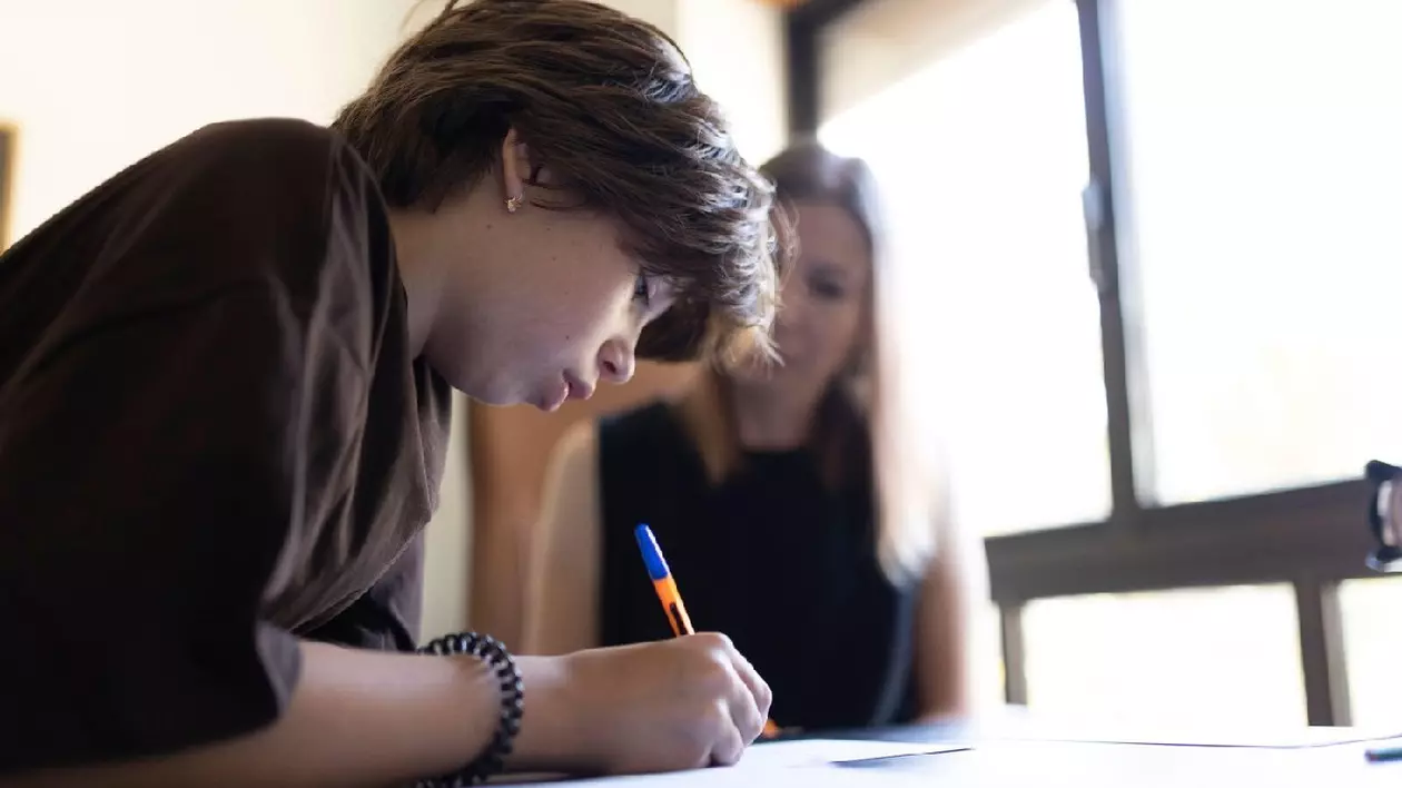 Elev care se concentrează asupra testului, scriind pe hârtie, cu ajutorul profesorului