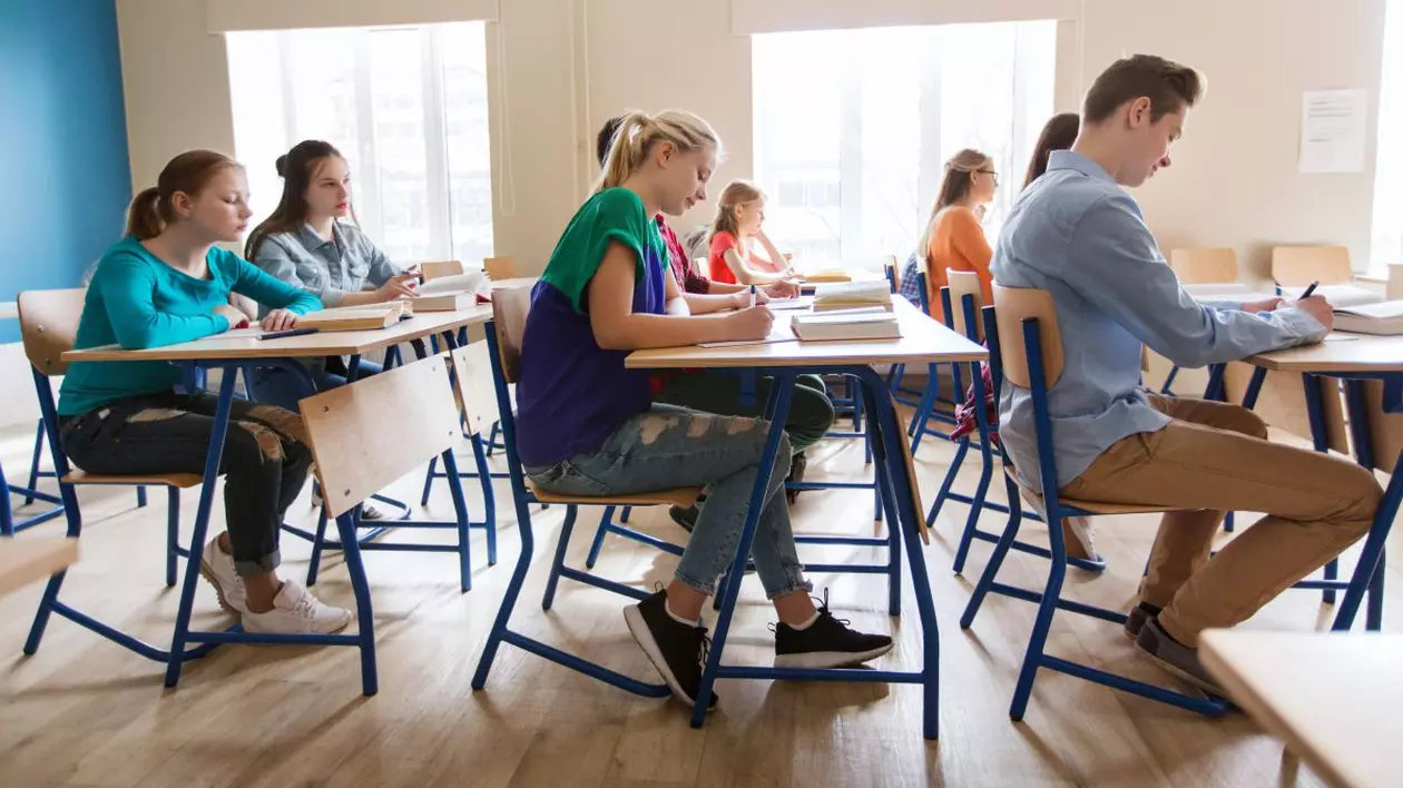 6 elevi în bănci susțin un examen, stau pe scaun și scriu.