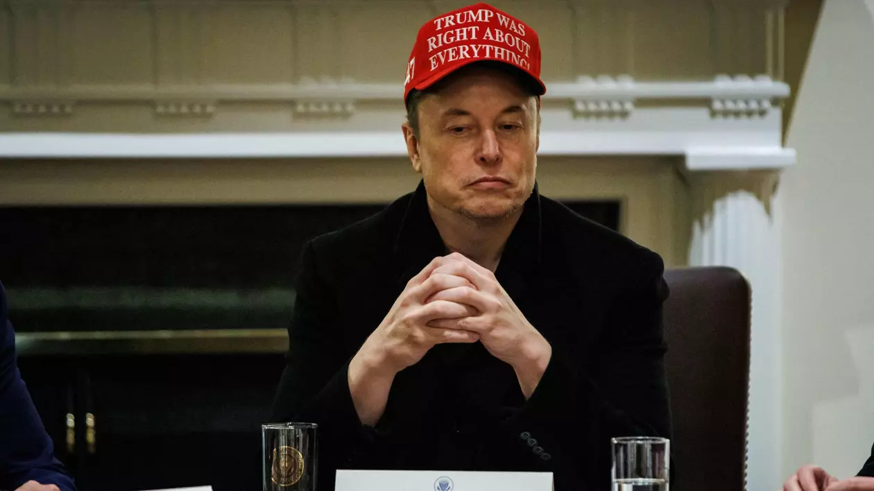 Elon Musk surprins în timp ce stă la masă. Poartă o șapcă roșie pe care scrie „Trump a avut dreptate în toate privințele”