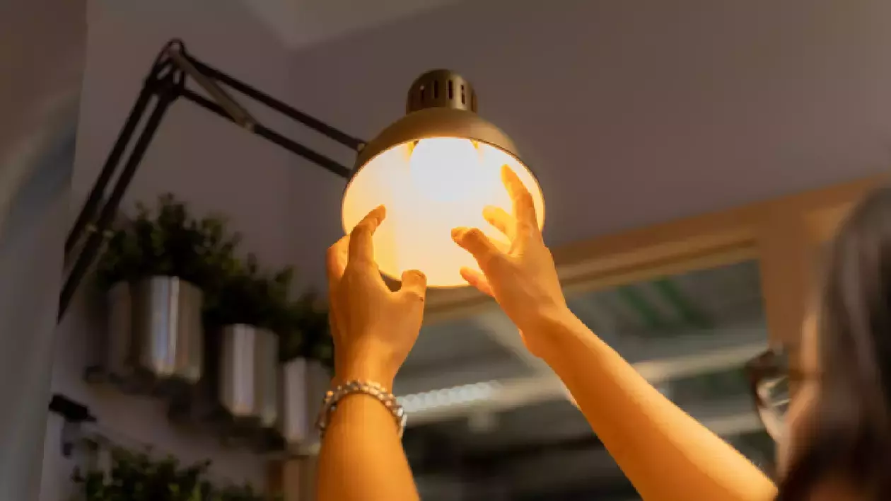 O femeie înșurubează un bec cu mâinile într-o veioză și se vede lumina