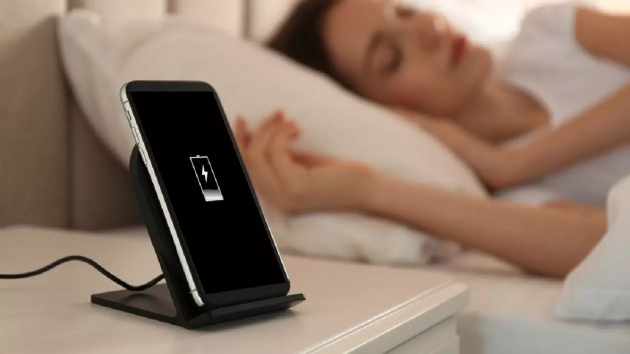 De ce nu este bine să lași telefonul la încărcat noaptea - Imagine cu o femeie care doarme având lângă cap un telefon la încărcat, pe o noptieră
