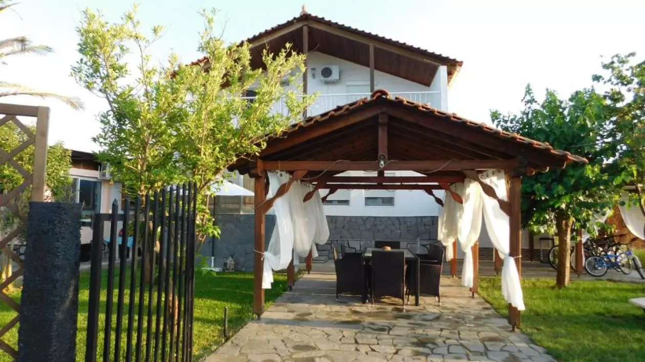 Casa Ferienhaus din Halkidiki, Grecia, cu un foișor în fața casei, iar pe fundal casa de culoare albă și acoperiș de lemn