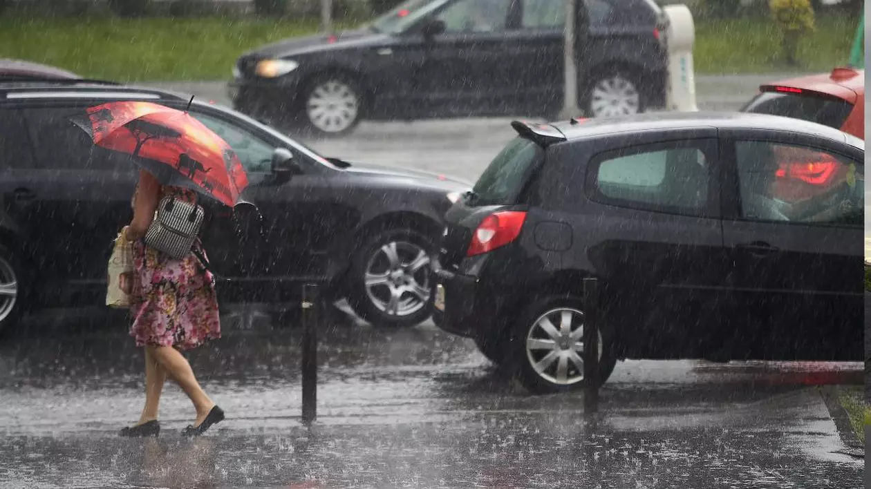 Mașinile din București blocate de o ploaie torențială de vară și o femeie în rochie, cu umbrelă, încearcă să traverseze.