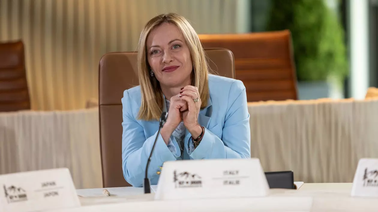 Giorgia Meloni, imbracata intr-un taior bleu, surprinsă zâmbind și având mâinile împreunate în timpul summitului G7