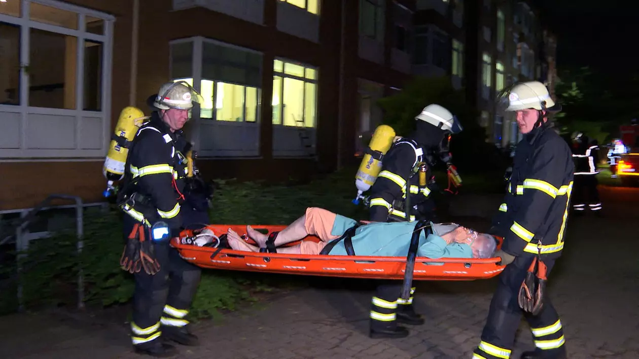 doi pompieri cara pe o targa o persoana ranita in urma unui incendiu la un spital din Hamburg. un al treilea pompier acorda ingrijiri pacientului