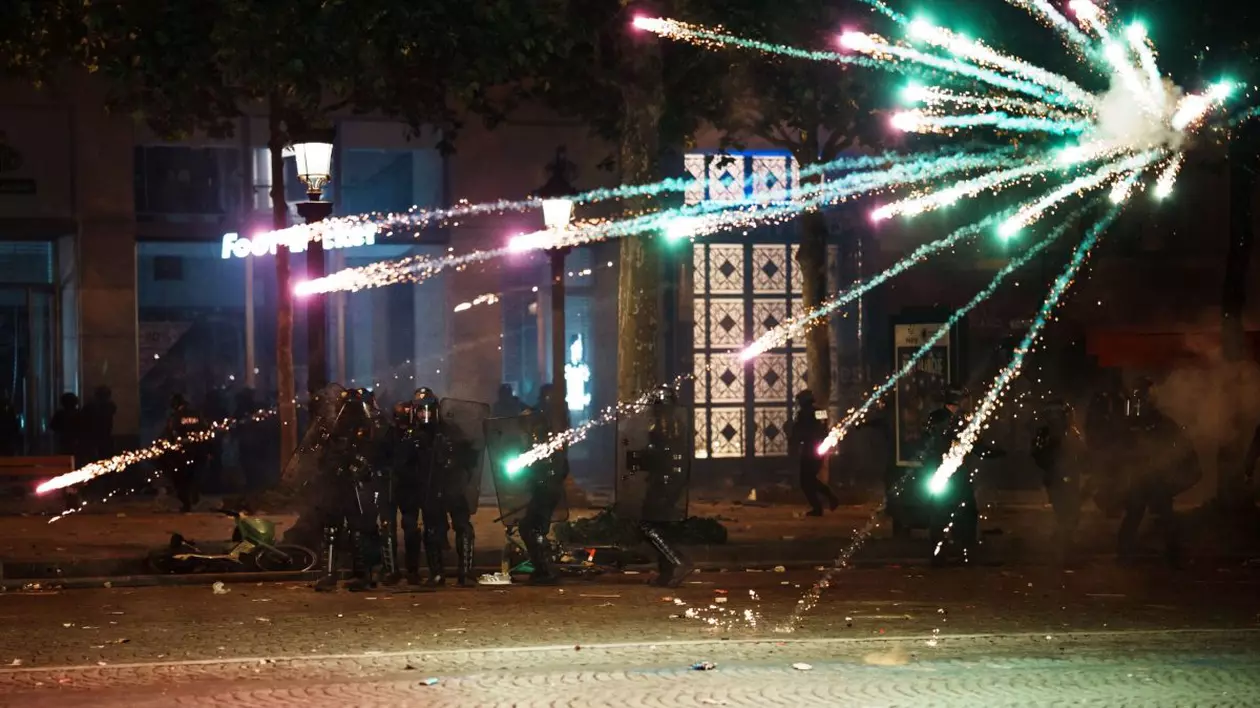 Poliția din Paris, luminată de focul unui artificiu care explodează în apropierea lor.
