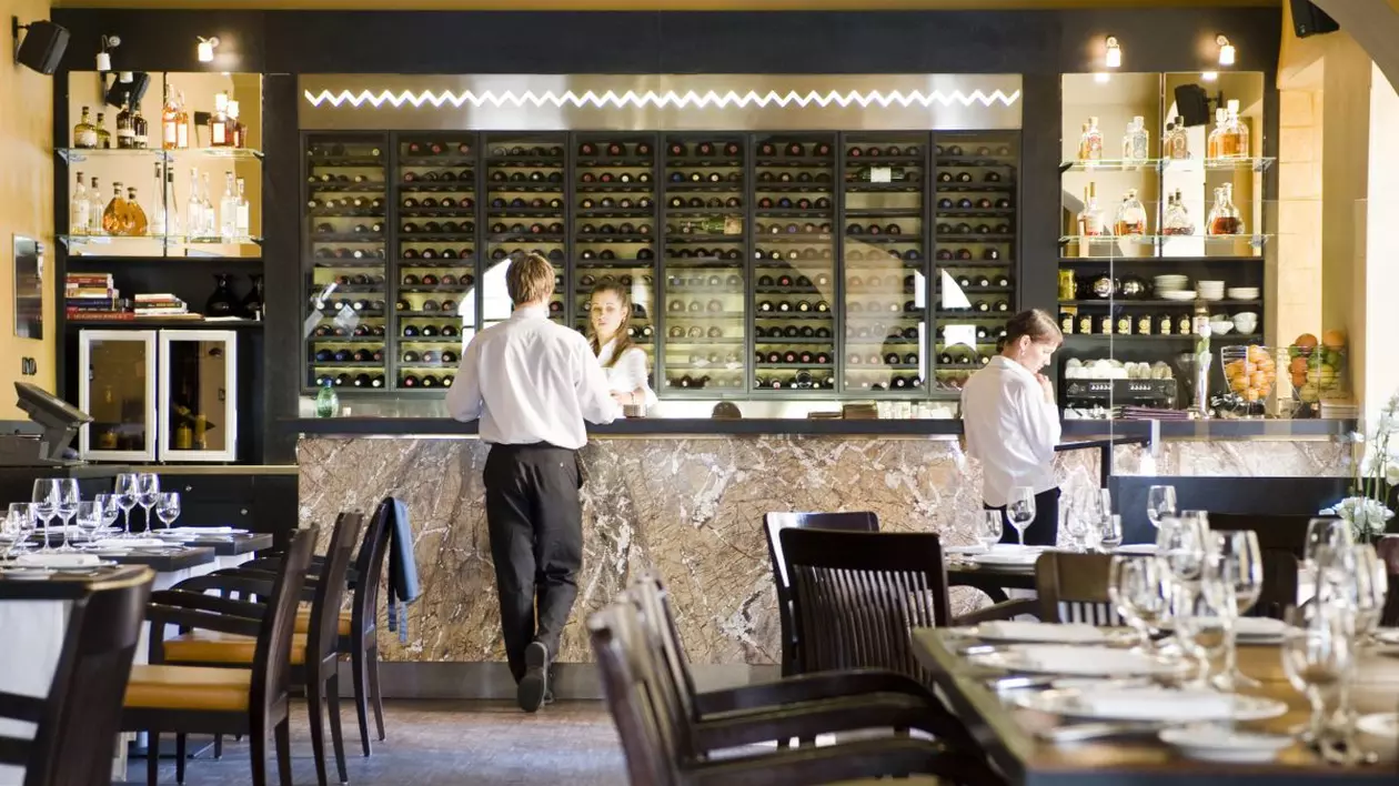 Interiorul unui restaurant din Cehia, chelneri așteaptă la bar sau se plimbă prin sală.