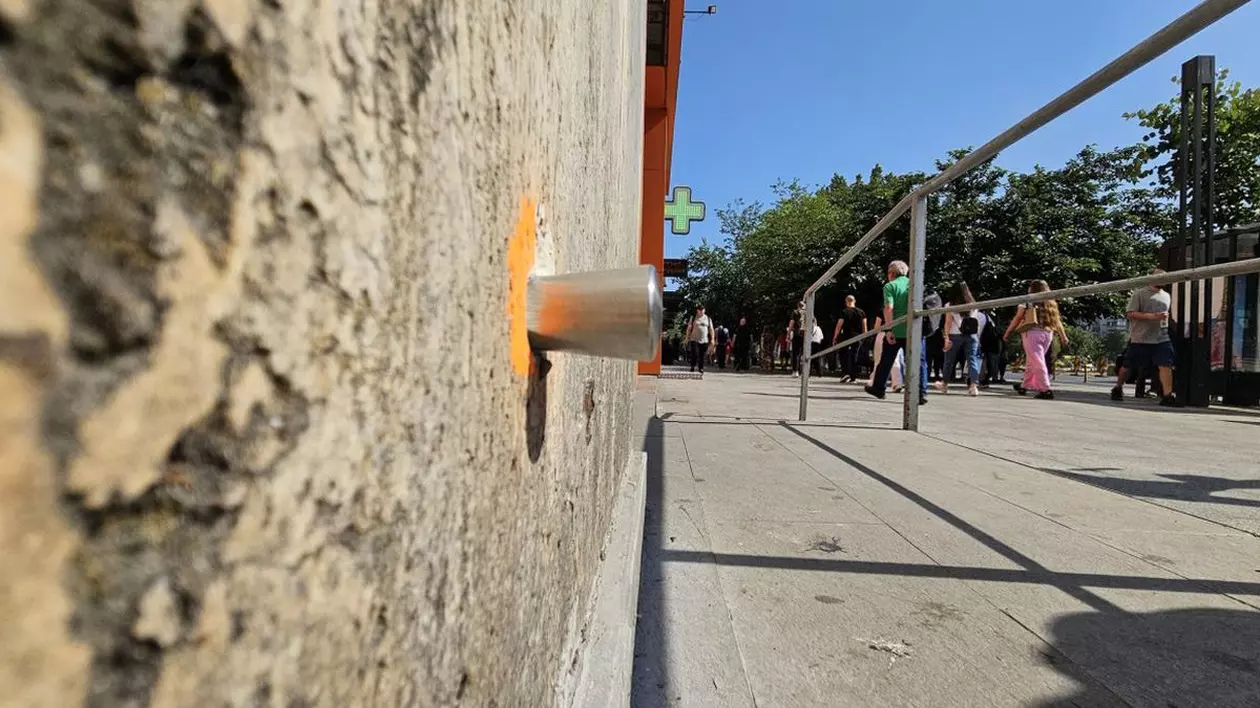 În partea stângă este un senzor montat pe peretele unei clădiri vechi, care monitorizează lucrările care au început la planșeul Unirii, în partea dreaptă sunt oameni care merg pe stradă într-o zi caldă de vară, se vede o bară metalică și semnul unei farmacii