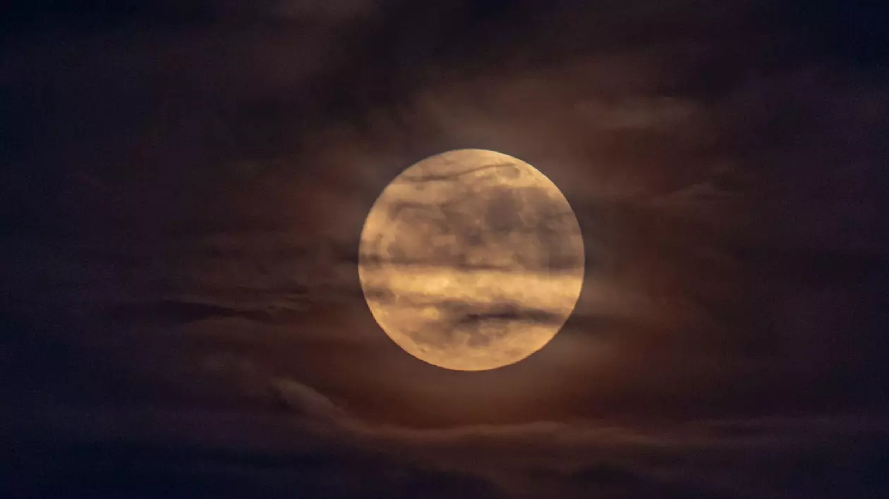 O lună plină aurie răsărind printre nori noaptea