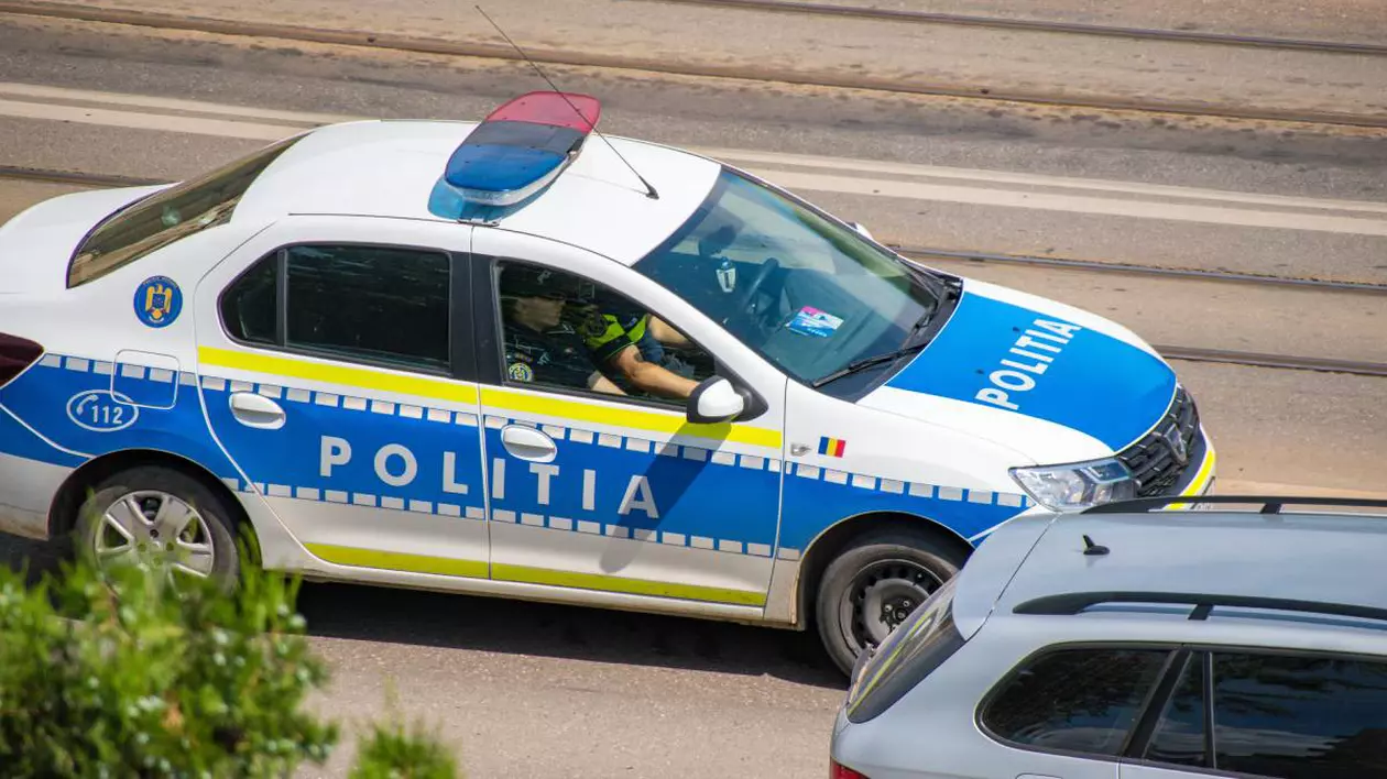 O mașină de Poliție în care stau doi polițiști în uniformă este parcată pe marginea drumului.