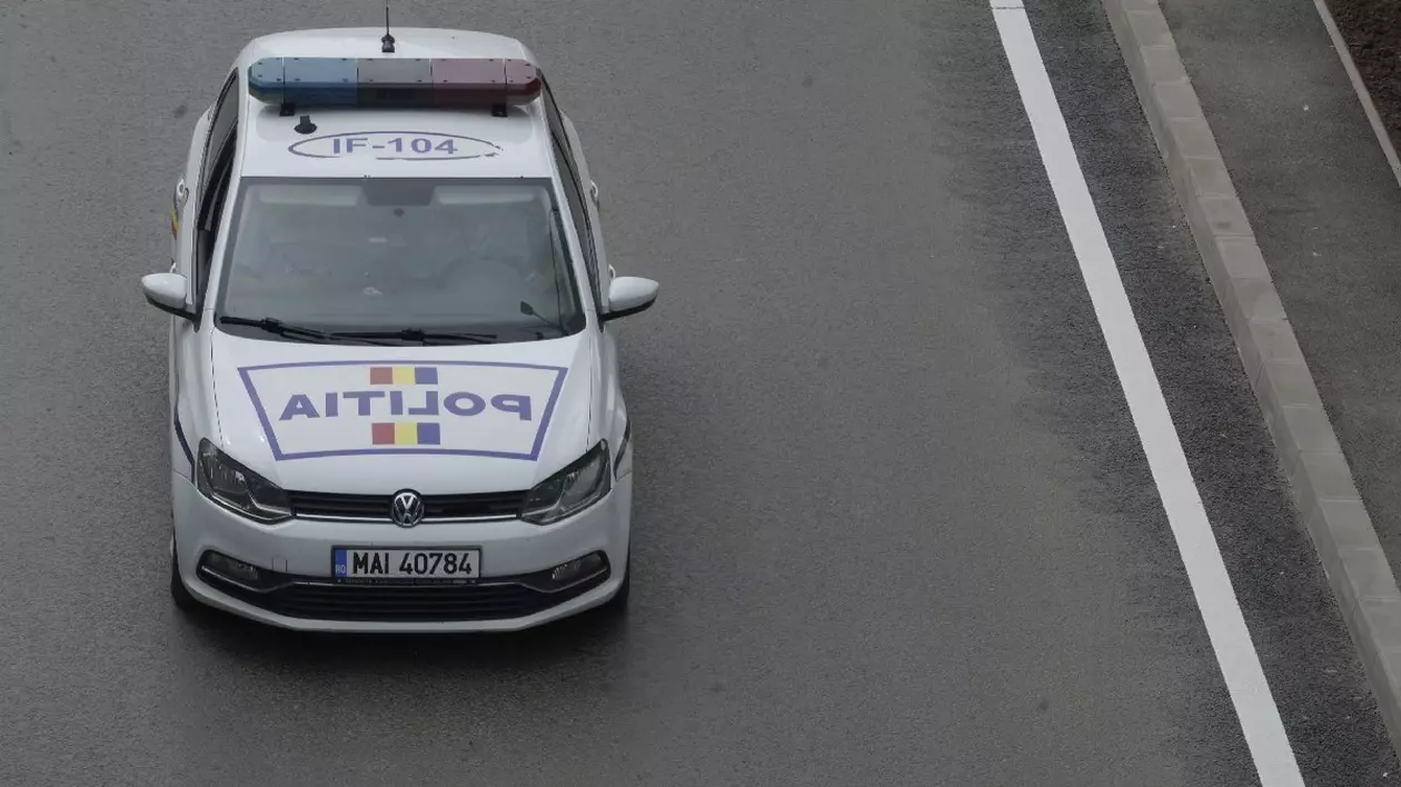 O mașină albă ce aparține Poliției Române circulă pe o șosea