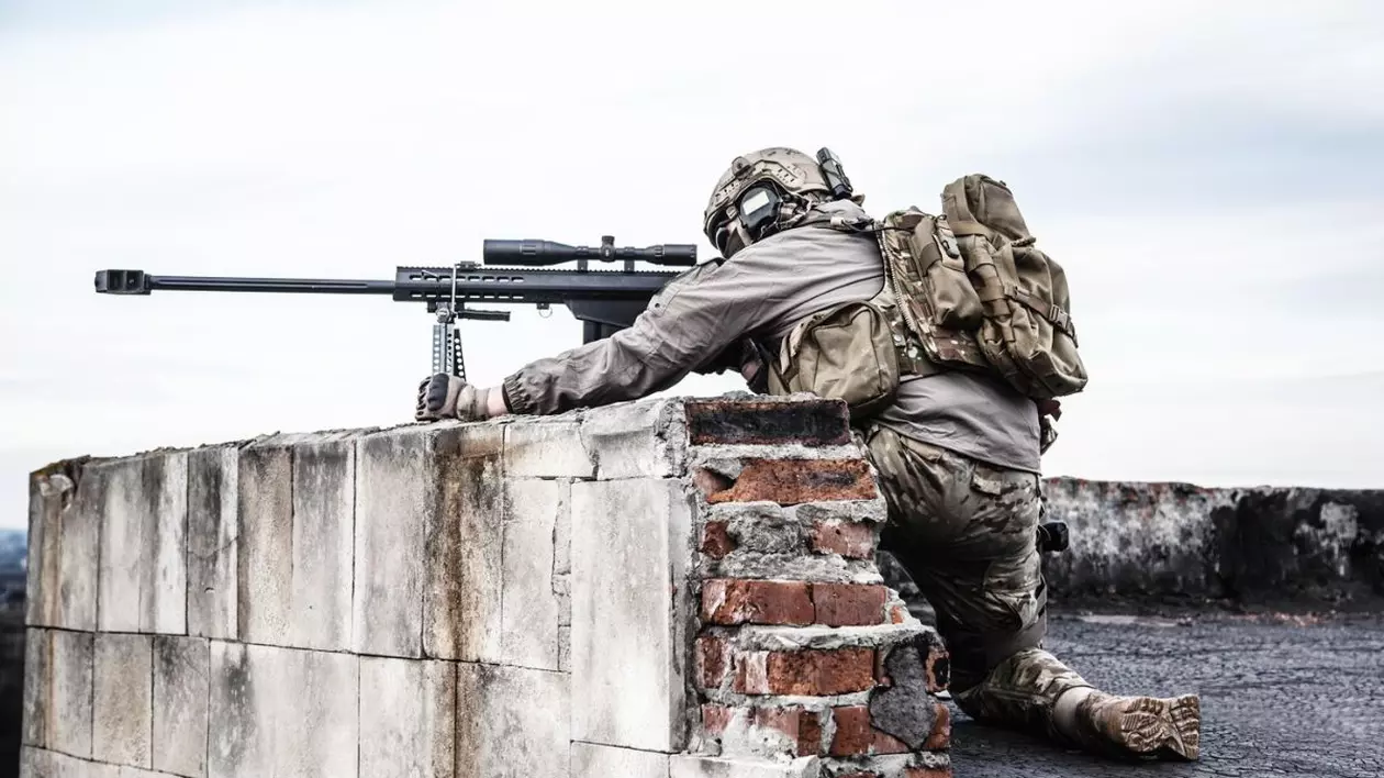 militar american care trage cu o pușcă tip sniper din spatele unui zid scurt de cărămidă în timpul unui exercițiu militar