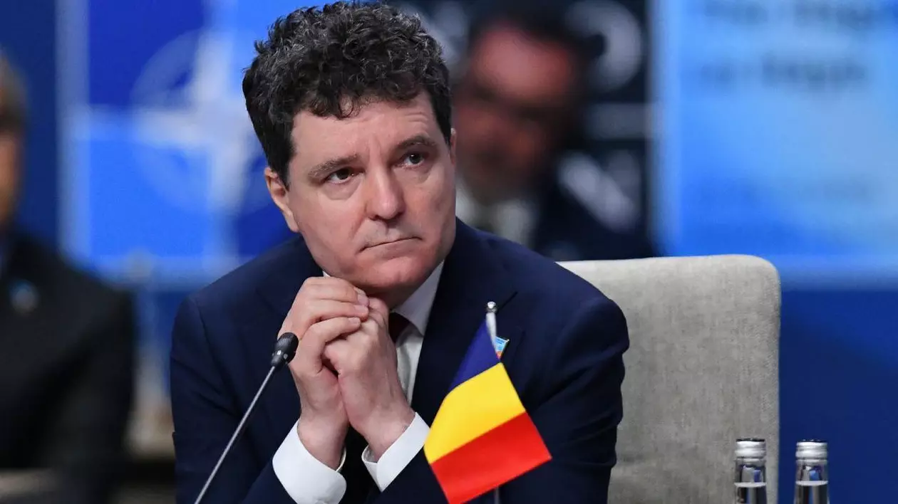 Președintele Nicușor Dan , așezat, cu mâinile impreunate la falcă, cu steagul României langă el, la Intalnirea Consiliului Nord Atlantic in cadrul summitului NATO 2025, in Haga, Tarile de Jos, 25 iunie 2025.