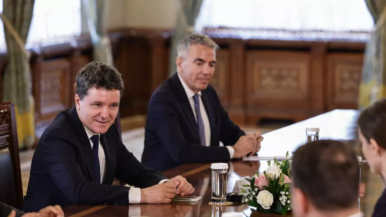Președintele Nicușor Dan, în timpul negocierilor de joi de la Palatul Cotroceni, stă la masa cu alți politicieni români, îmbrăcat la costum și zâmbește